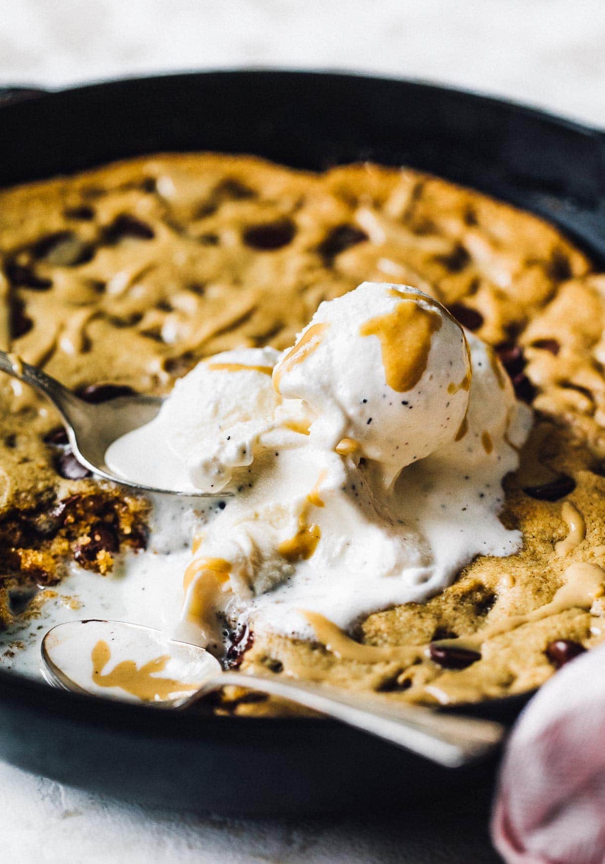 close up of chocolate chip cookie in a skillet with vanilla ice cream scoops