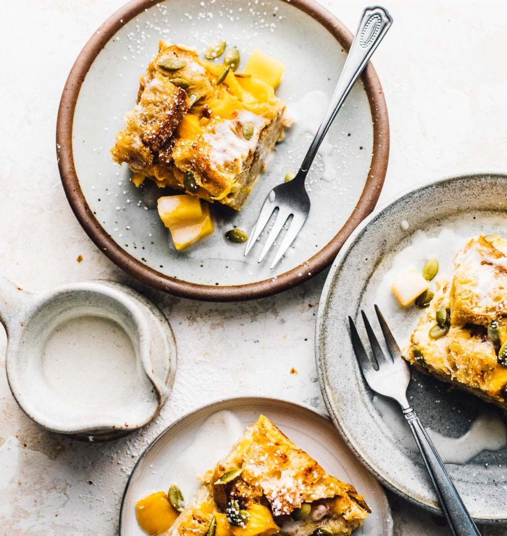 mango bread pudding on 3 small plates with pitcher of cream to the left