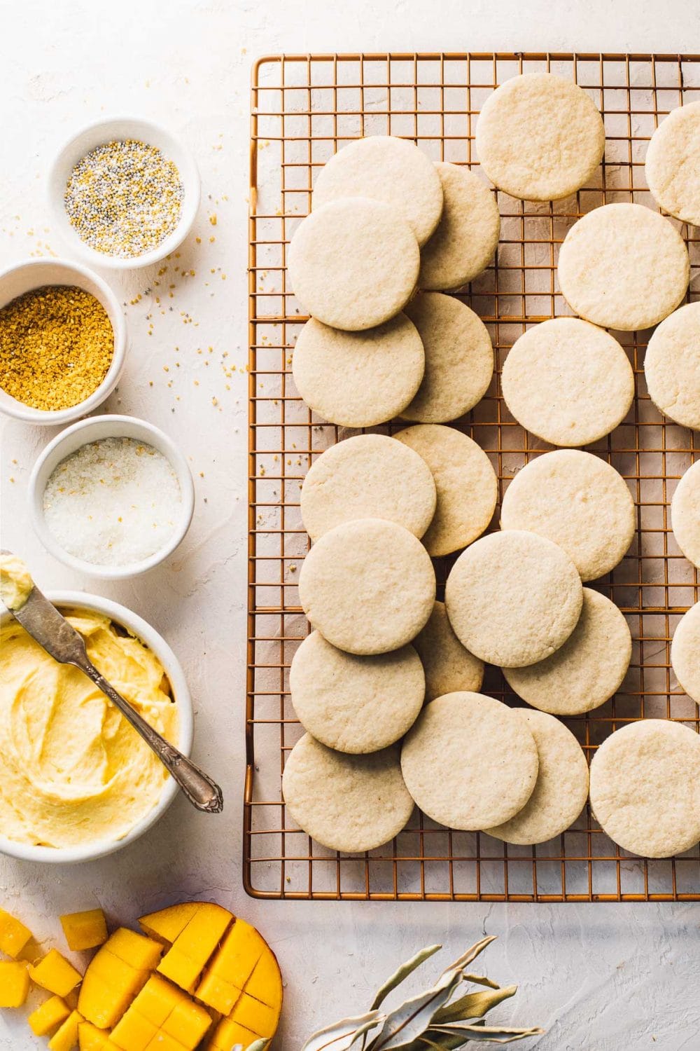 gluten free sugar cookies on wire cooling rack with white and gold sprinkles, and frosting, in bowls to the left of the cookies
