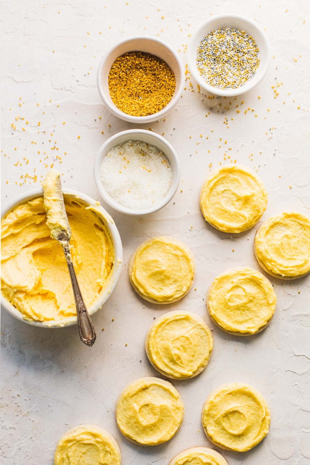 frosted sugar cookies with sprinkles in small dishes next to them