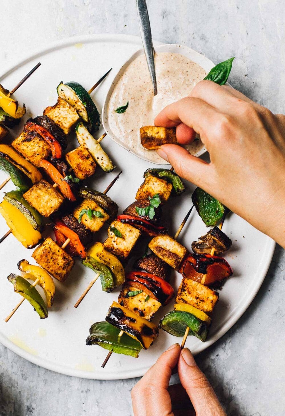 woman dipping tofu from a veggie skewer into dipping sauce