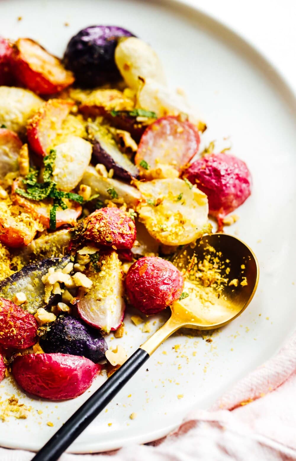 roasted radishes on white plate with gold and black spoon
