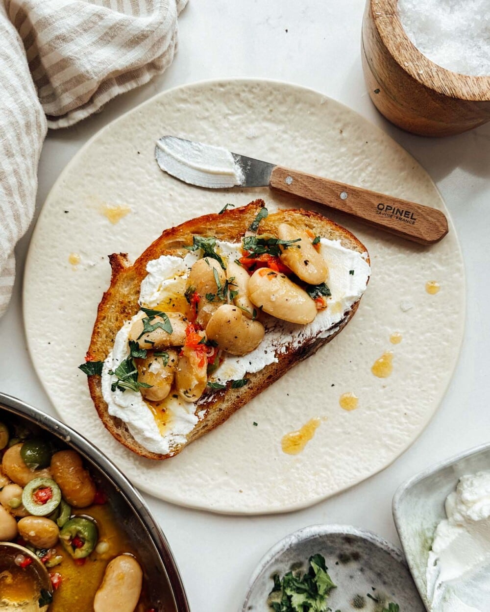 Marinated Gigante Beans on toast with ricotta cheese, on a cream colored plate.