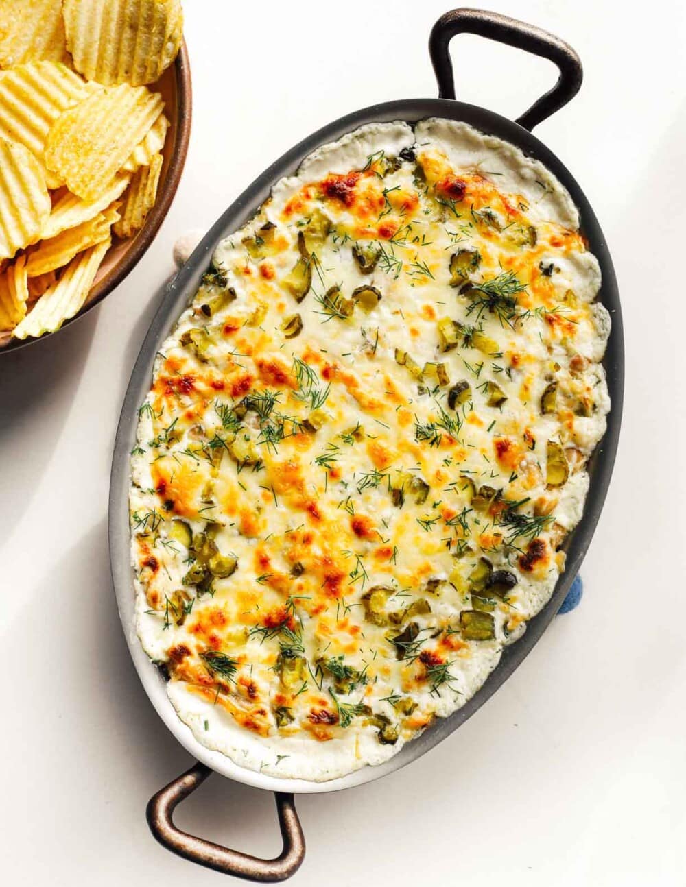baked ranch pickle dip in a casserole dish with bowl of chips to its left