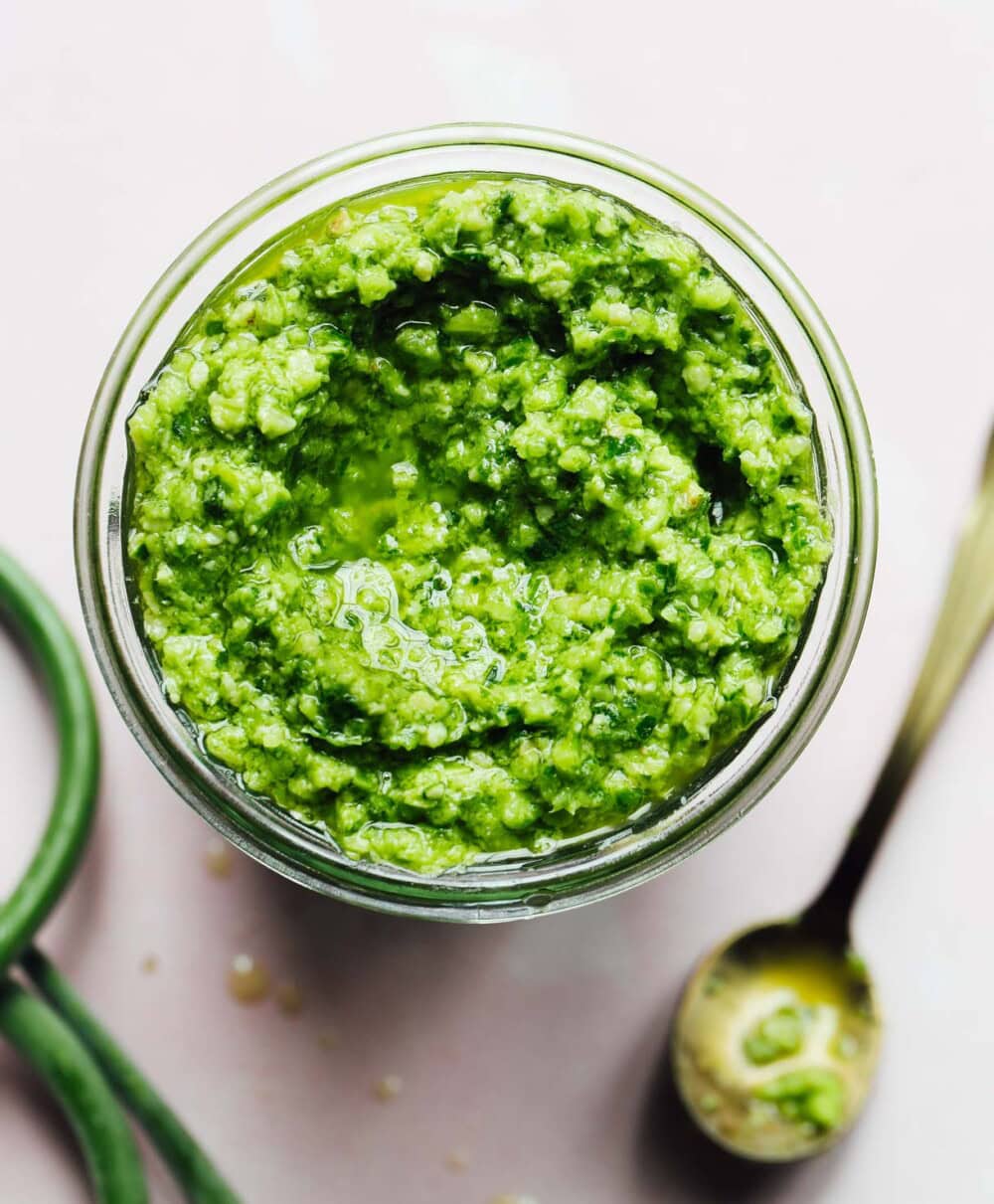 garlic scape pesto in jar with gold spoon to its right