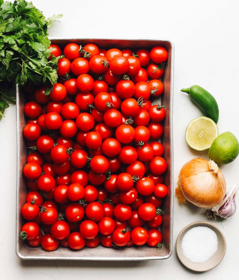 cherry tomatoes in a pan with cilantro, jalapeno, lime, onion to its right