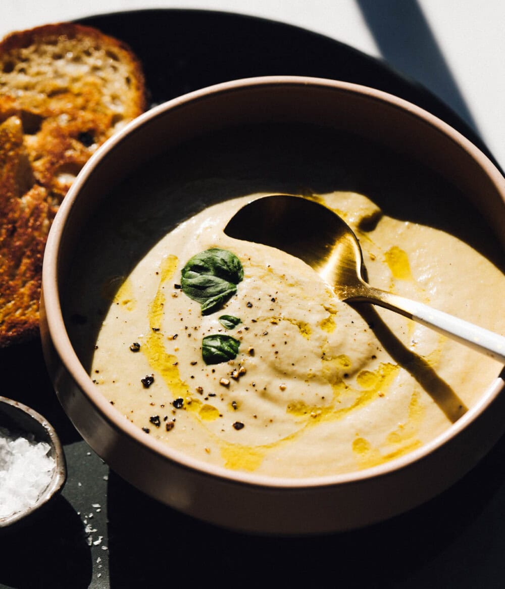 green tomato soup in a pink bowl with pieces of sourdough toast to the left. 