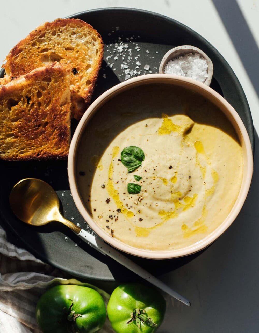 green tomato soup in a bowl with sourdough toast to its left. 